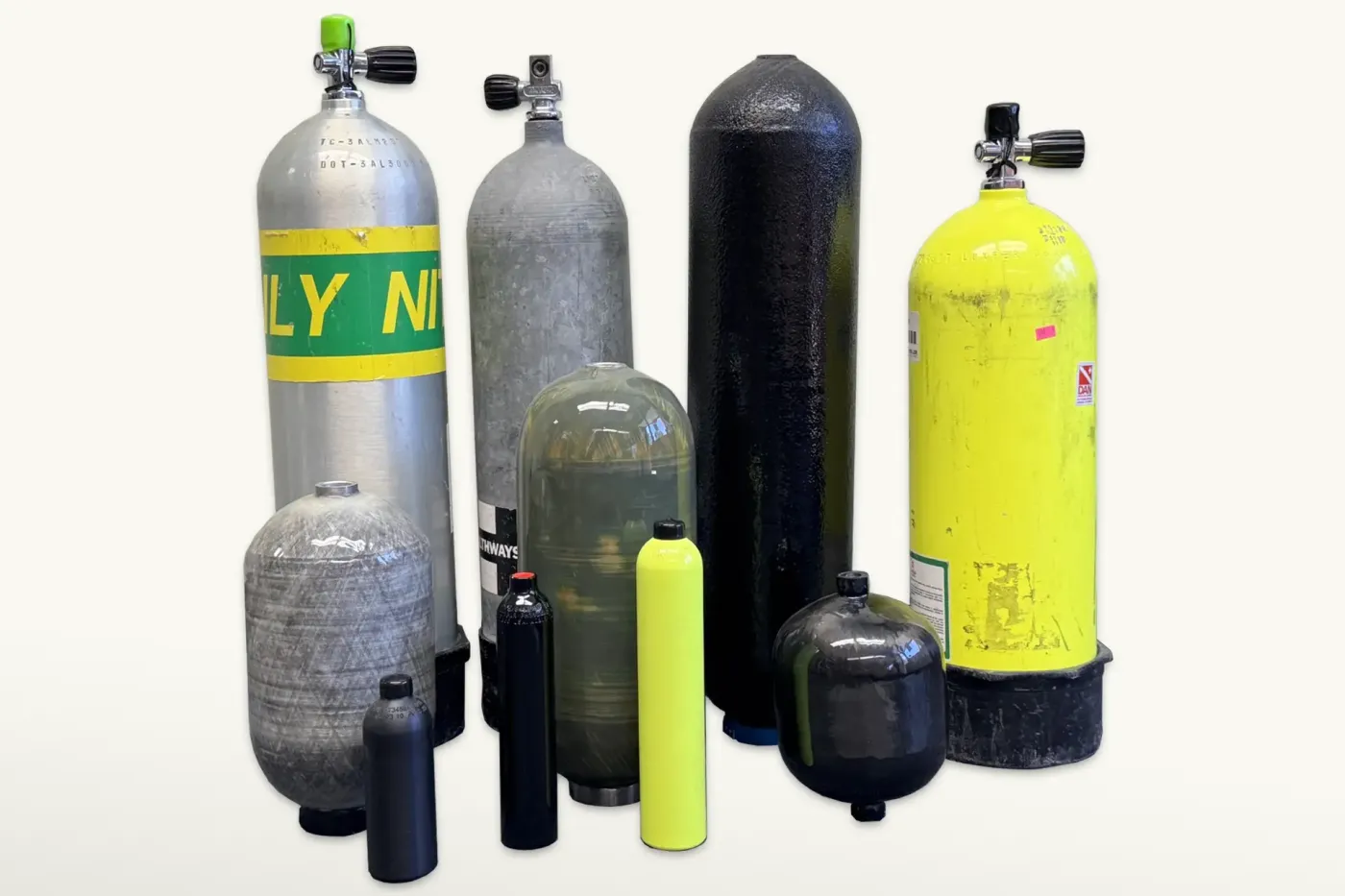 Assorted composite and metal pressure vessels prepared for visual inspection, showing variations in size, material, and condition before recertification.
