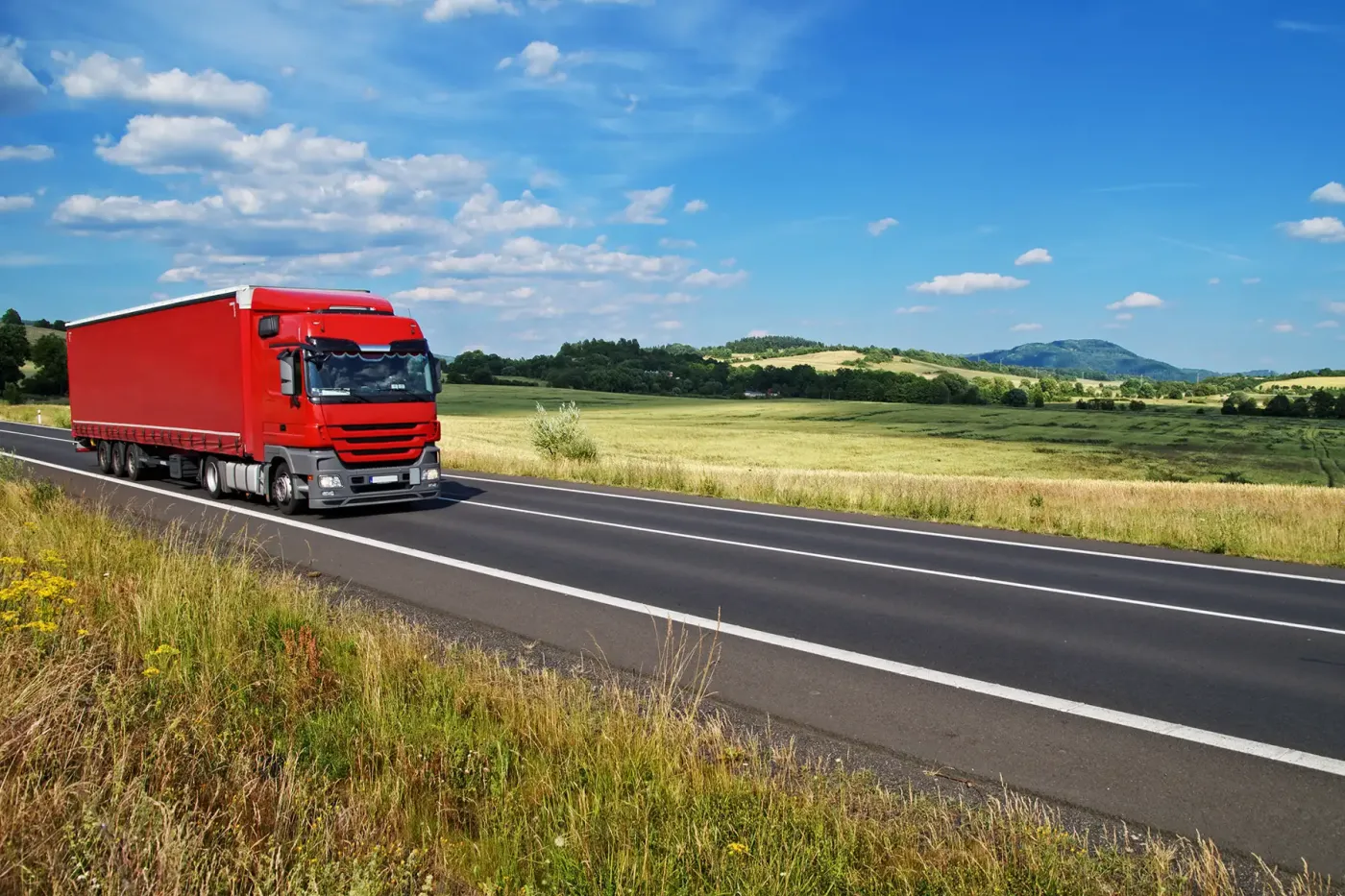 Red heavy-duty truck driving on a highway through open countryside, representing clean transportation and fleet applications powered by compressed natural gas or hydrogen storage solutions.